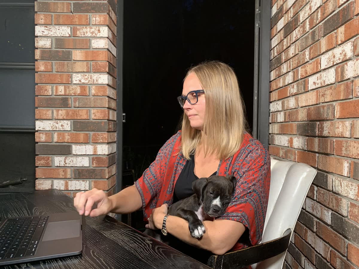 Mandie Jones at a laptop on a brick porch, a puppy asleep in her lap